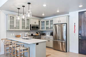 Kitchen featuring stainless steel appliances, tasteful backsplash, a peninsula, light wood-type flooring, and a kitchen breakfast bar