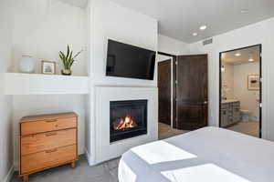 Bedroom featuring light colored carpet, a glass covered fireplace, recessed lighting, and connected bathroom