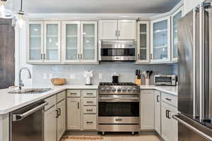 Kitchen with premium appliances, tasteful backsplash, hanging light fixtures, light stone counters, and a peninsula