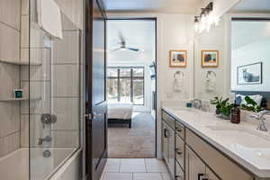 Ensuite bathroom with  shower combination, double vanity, light colored carpet, light tile patterned floors, and a ceiling fan