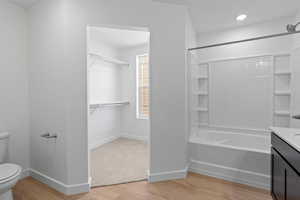 Full bathroom with light wood-type flooring, vanity, tub / shower combination, and a walk in closet