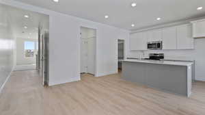 Kitchen with recessed lighting, white cabinetry, an island with sink, appliances with stainless steel finishes, and light wood finished floors