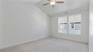 Empty room featuring light carpet, lofted ceiling, and a ceiling fan