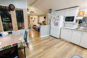 Kitchen featuring white cabinetry, freestanding refrigerator, light countertops, light wood-type flooring, and vaulted ceiling