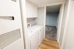 Laundry area featuring a heating unit, light wood-type flooring, washer and clothes dryer, and cabinet space