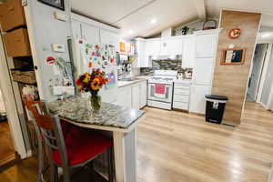Kitchen featuring light wood-style floors, a kitchen bar, white appliances, decorative backsplash, and white cabinetry