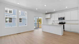 Kitchen featuring white cabinets, stainless steel appliances, a kitchen island with sink, recessed lighting, and light wood-style flooring