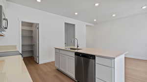 Kitchen featuring appliances with stainless steel finishes, recessed lighting, a center island with sink, light wood-style floors, and white cabinets