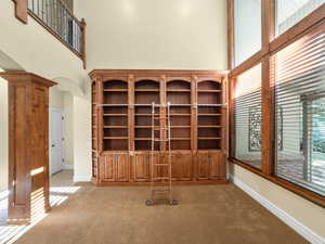 Unfurnished living room featuring a high ceiling, light colored carpet, arched walkways, and decorative columns