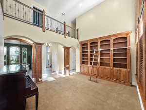 Unfurnished living room with a towering ceiling, arched walkways, ornate columns, and light colored carpet
