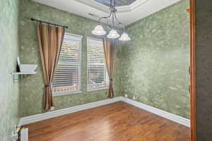 Unfurnished dining area with wood finished floors, a raised ceiling, and a chandelier