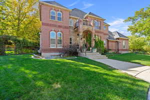 View of front of property with brick siding, a front lawn, a shingled roof, and a balcony