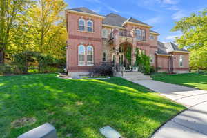 View of front of home with brick siding, a front yard, a balcony, and roof with shingles
