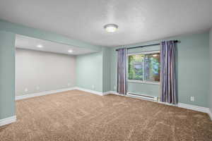 Spare room with a baseboard heating unit, a textured ceiling, and carpet