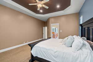 Carpeted bedroom featuring a tray ceiling, ceiling fan, recessed lighting, crown molding, and connected bathroom