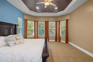 Carpeted bedroom with ornamental molding, ceiling fan, recessed lighting, and a tray ceiling