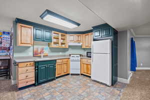 Kitchen with glass insert cabinets, white appliances, light countertops, under cabinet range hood, and light stone finish floors