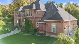 French country inspired facade with a front yard, brick siding, a shingled roof, and an attached garage