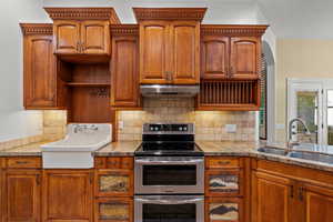 Kitchen featuring double oven range, brown cabinetry, decorative backsplash, and under cabinet range hood