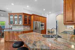 Kitchen featuring a peninsula, glass insert cabinets, a kitchen breakfast bar, light stone counters, and recessed lighting