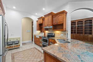 Kitchen featuring inlaid floor details, light tile patterned floors, stainless steel appliances, brown cabinets, and recessed lighting