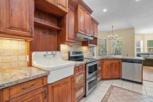 Kitchen featuring light tile patterned floors, appliances with stainless steel finishes, brown cabinets, tasteful backsplash, and a chandelier