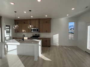 Kitchen featuring stainless steel appliances, brown cabinets, hanging light fixtures, backsplash, and light wood-style flooring