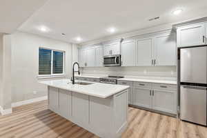 Kitchen featuring appliances with stainless steel finishes, light wood finished floors, light stone countertops, a center island with sink, and recessed lighting