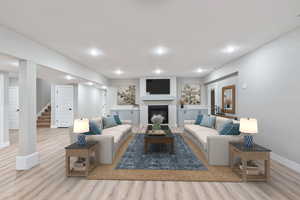 Living room with light wood-style floors, a glass covered fireplace, stairway, and recessed lighting