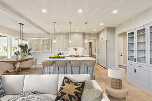Kitchen featuring beamed ceiling, gray cabinetry, a breakfast bar area, recessed lighting, and a center island with sink