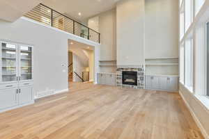 Unfurnished living room featuring healthy amount of natural light, a towering ceiling, a stone fireplace, light wood finished floors, and recessed lighting