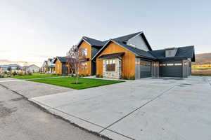 Modern inspired farmhouse featuring concrete driveway, a garage, a shingled roof, a front lawn, and board and batten siding