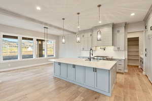 Kitchen featuring gray cabinets, beam ceiling, an island with sink, pendant lighting, and light wood-style flooring