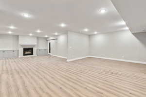 Unfurnished living room with light wood-type flooring, a glass covered fireplace, and recessed lighting