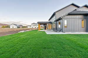 Rear view of house with board and batten siding, a lawn, a patio area, and a shingled roof