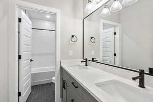 Full bathroom featuring double vanity, shower / bath combination, and dark tile patterned floors