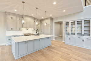 Kitchen featuring gray cabinets, decorative light fixtures, a kitchen island with sink, light stone counters, and recessed lighting