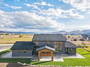 Rear view of property with a patio, roof with shingles, a mountain view, and a lawn