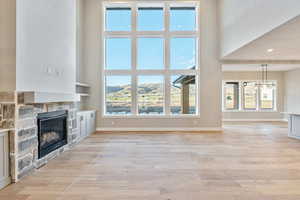 Unfurnished living room with a stone fireplace, light wood finished floors, a high ceiling, a mountain view, and a chandelier