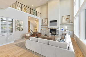Living room featuring a high ceiling, light wood finished floors, built in features, a stone fireplace, and recessed lighting