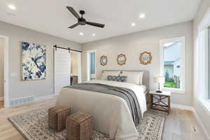 Bedroom featuring a barn door, light wood-style flooring, recessed lighting, ceiling fan, and connected bathroom