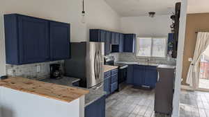 Kitchen with blue cabinets, stainless steel appliances, decorative light fixtures, butcher block countertops, and a peninsula