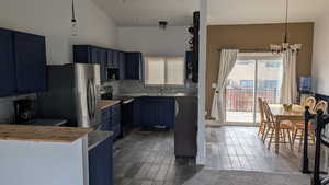 Kitchen with stainless steel appliances, decorative backsplash, blue cabinets, and healthy amount of natural light