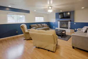 Living room with recessed lighting, light wood finished floors, a fireplace, ceiling fan, and a textured ceiling