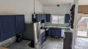 Kitchen featuring backsplash, stainless steel appliances, blue cabinetry, and light countertops