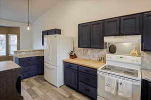 Kitchen with white appliances, decorative backsplash, pendant lighting, under cabinet range hood, and vaulted ceiling