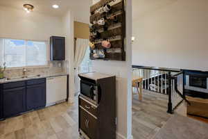 Kitchen with wood tiled floors, white dishwasher, stainless steel microwave, and decorative backsplash