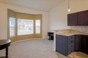 Kitchen featuring hanging light fixtures, tasteful backsplash, a peninsula, vaulted ceiling, and light carpet
