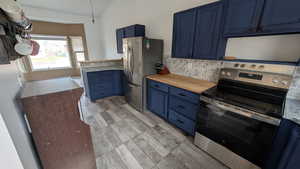 Kitchen with stainless steel appliances, blue cabinets, vaulted ceiling, backsplash, and wood tiled floors