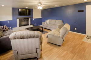 Living room with recessed lighting, wood finished floors, a fireplace, ceiling fan, and a textured ceiling